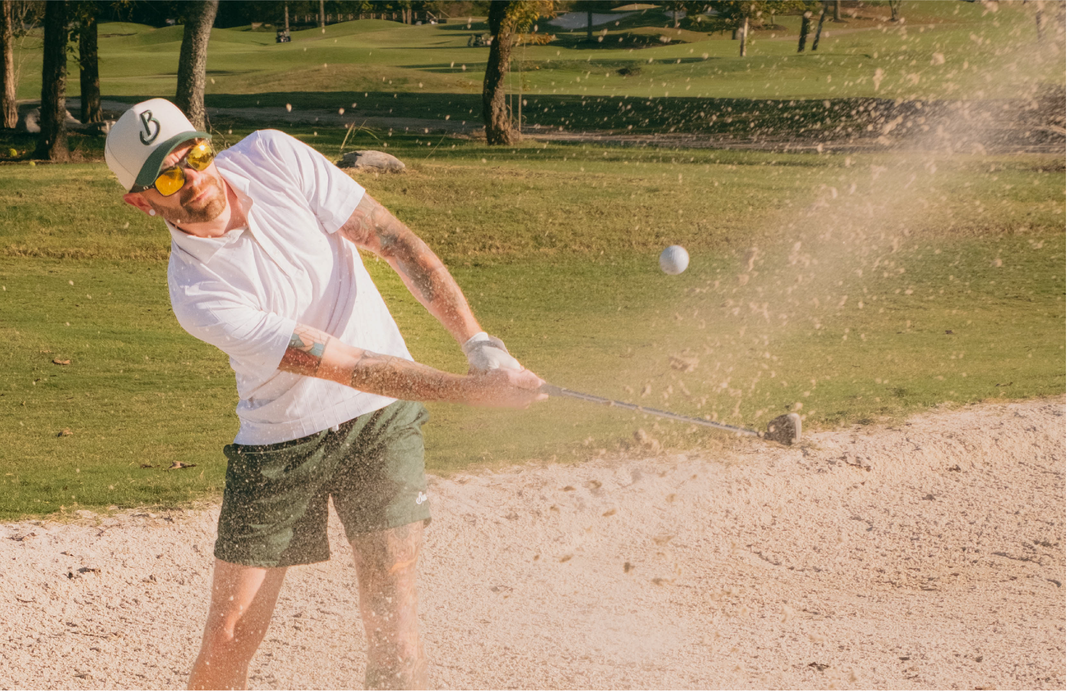 Man playing golf in a sand trap on a green course with trees in the background