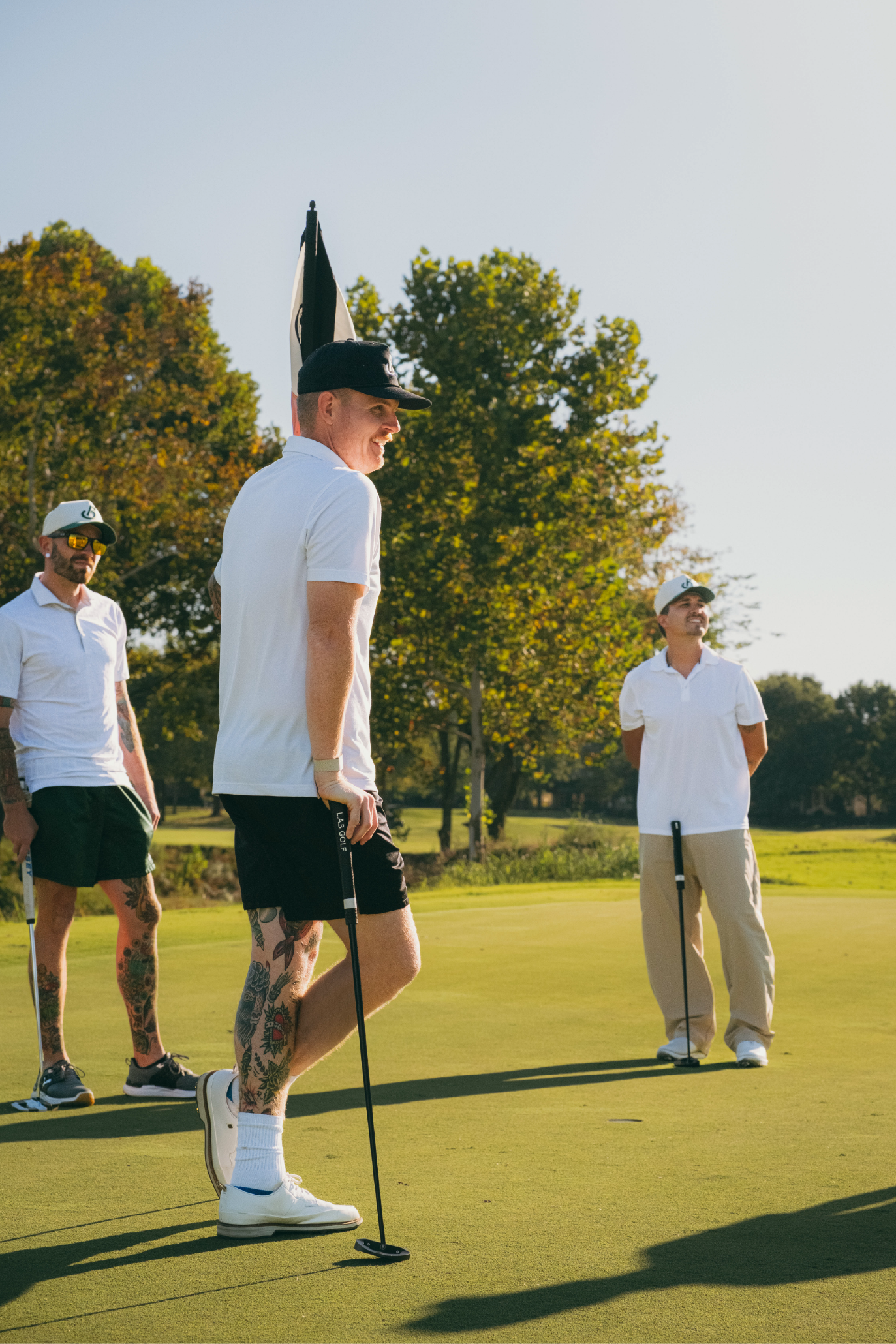 Three men playing golf on a sunny day with trees in the background